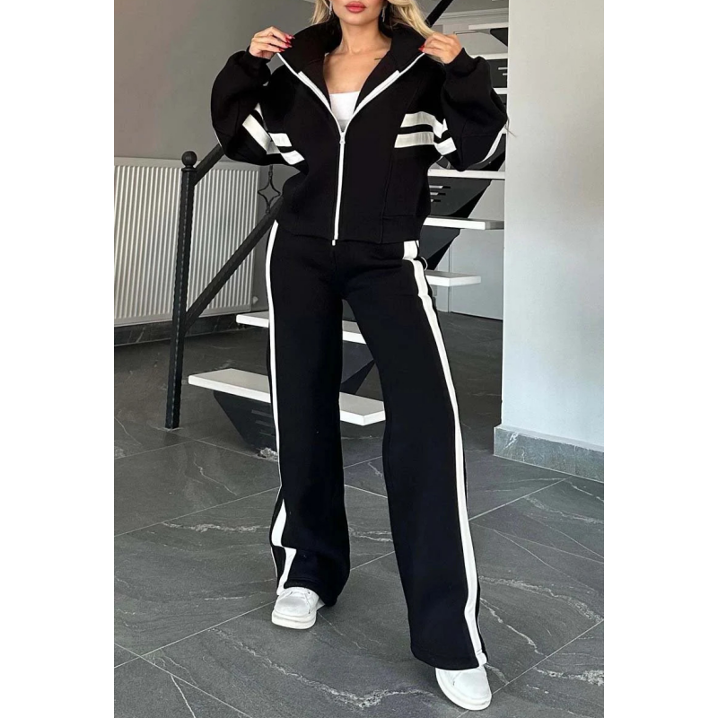 Model wearing the black set with white stripes, jacket zipped up with hands at the collar, full-length view of the trousers. 3