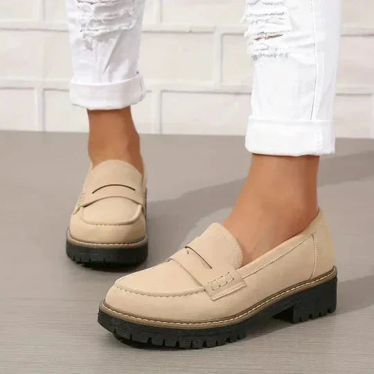 Beige loafers worn with white rolled jeans, one shoe in front and the other slightly behind, showing the stitched penny strap. 7