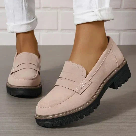 Soft pink-beige loafers with a chunky black sole, worn with white cuffed trousers, showing the stitched strap detail. 8