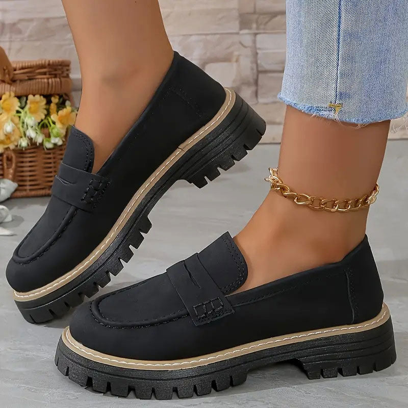 Black loafers with a tan welt stitch above the thick platform sole, worn with a gold chain anklet. 12