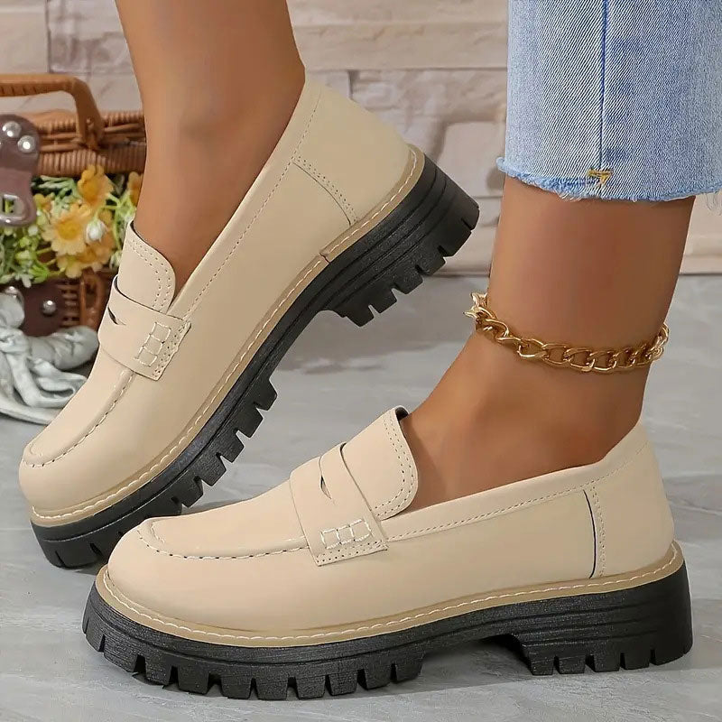 Cream smooth-finish loafers with a thick black platform sole and gold chain anklet, one foot lifted to show the side. 14