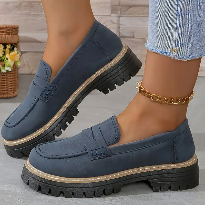 Navy blue suede-effect loafers with matching stitching on the strap and a thick black platform sole, worn with a gold anklet. 16
