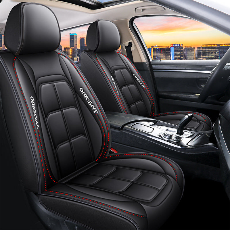 Pair of front car seat covers in black with red stitching, fitted to the seats, seen at an angle with a city sunset behind. 1