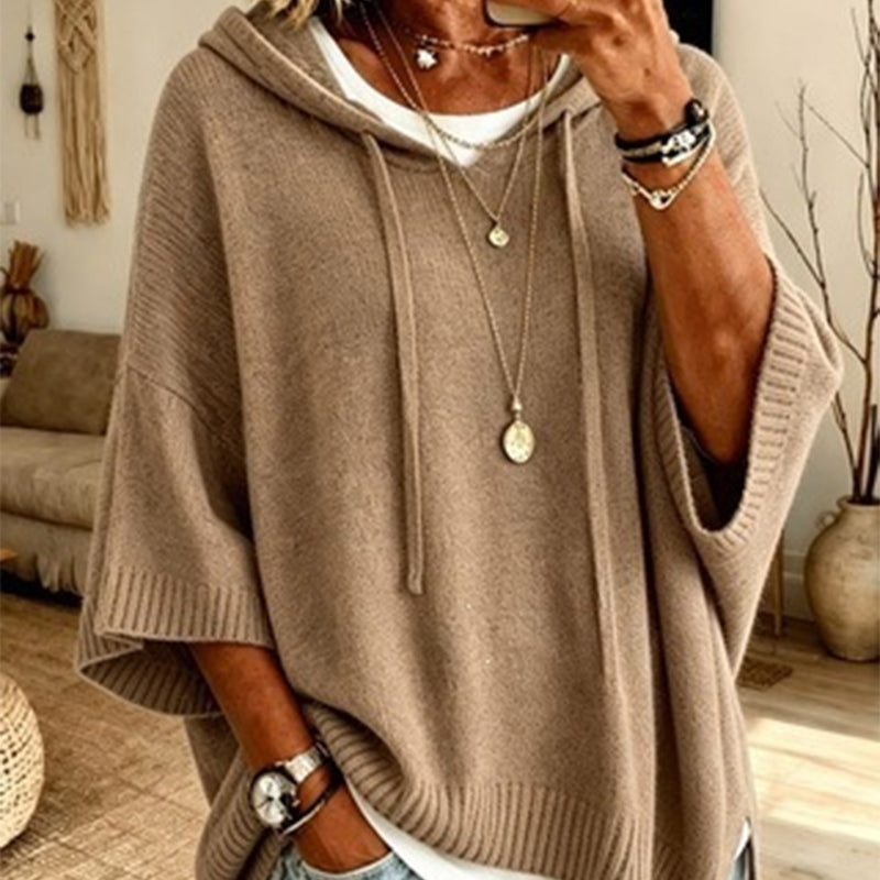 Close-up of the khaki hooded knit worn over a white top, with drawstrings, ribbed cuffs and layered necklaces. 14