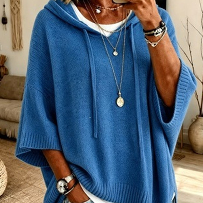 Close-up of the blue hooded knit worn over a white top, with drawstrings, ribbed cuffs and layered necklaces. 12