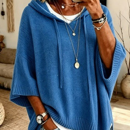 Close-up of the blue hooded knit worn over a white top, with drawstrings, ribbed cuffs and layered necklaces. 12