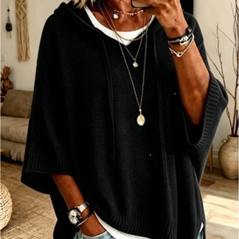 Close-up of the black hooded knit worn over a white top, with drawstrings, ribbed cuffs and layered necklaces. 10
