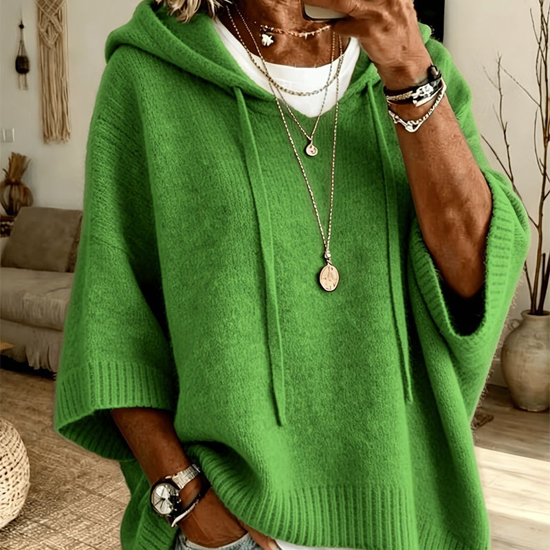 Close-up of the green hooded knit worn over a white top, with drawstrings, ribbed cuffs and layered necklaces. 19