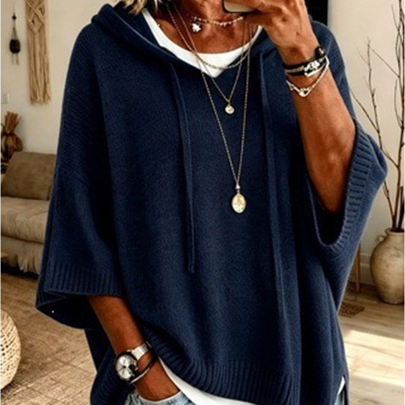 Close-up of the navy hooded knit worn over a white top, with drawstrings, ribbed cuffs and layered necklaces. 15