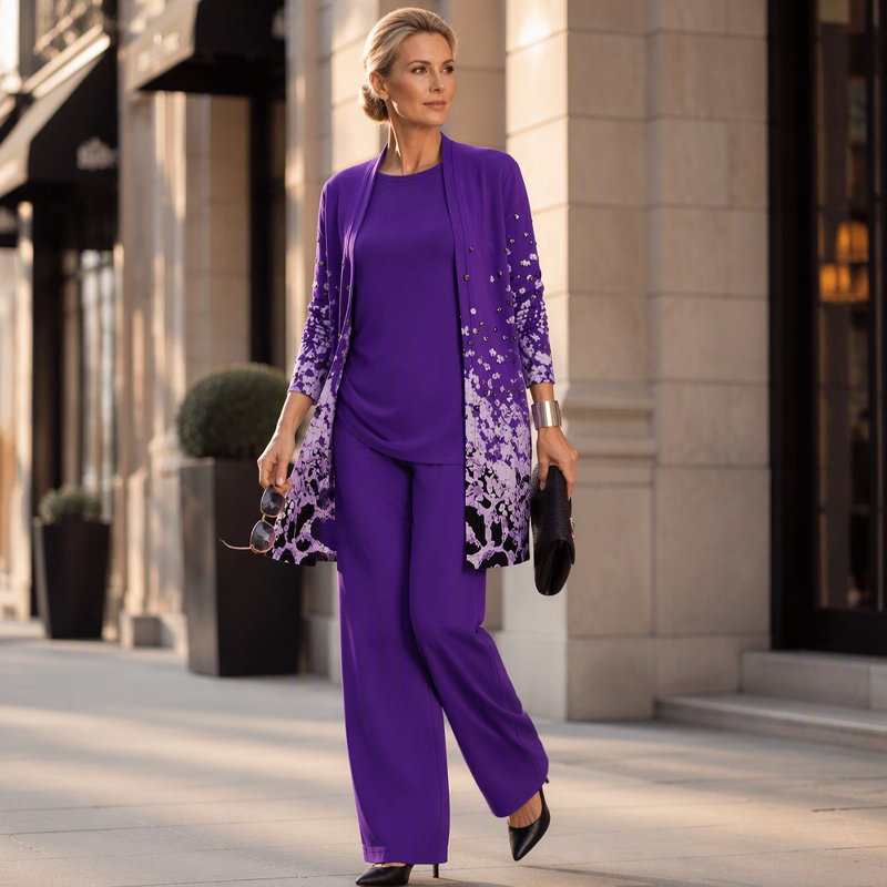 Woman walking along a city street in the purple set with black court shoes, holding sunglasses and a black clutch bag. 12