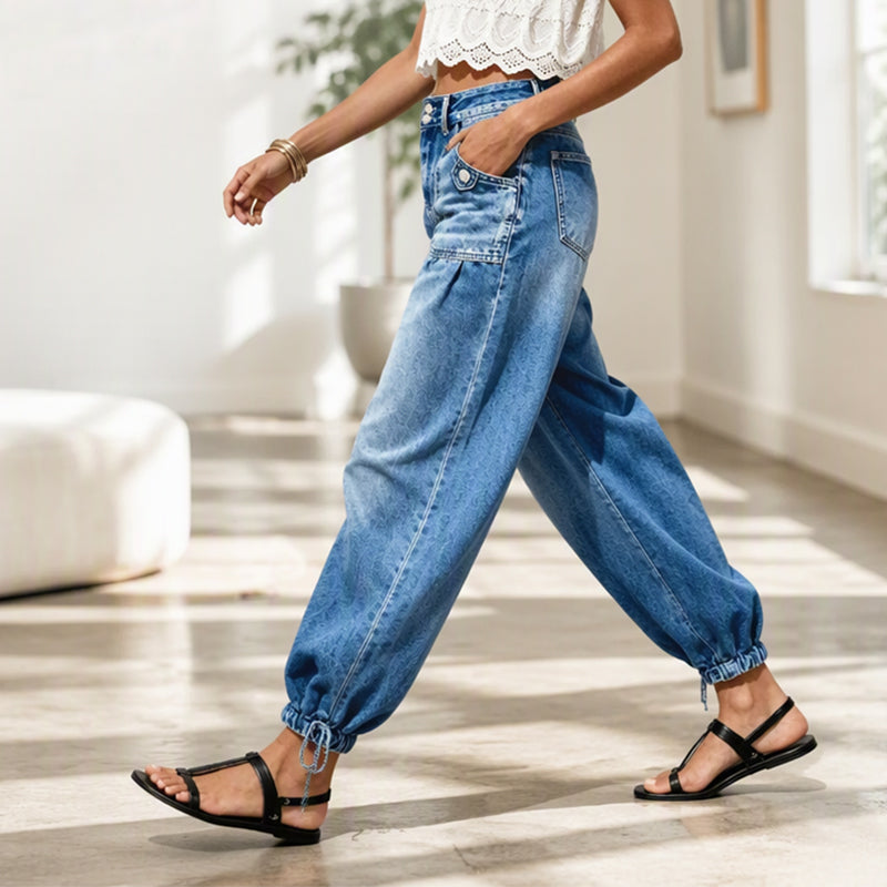 Side view of a model walking indoors in the blue jeans, showing the pleated hip, patch pocket and tied ankle hem. 7