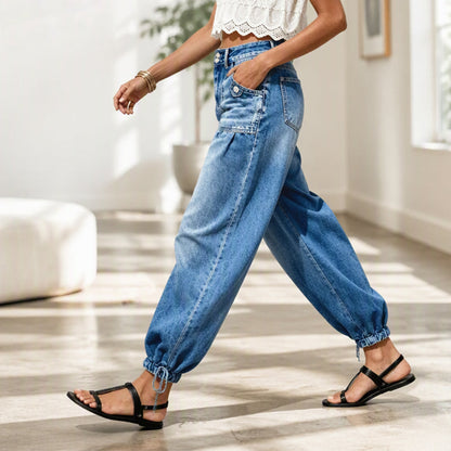 Side view of a model walking indoors in the blue jeans, showing the pleated hip, patch pocket and tied ankle hem. 7