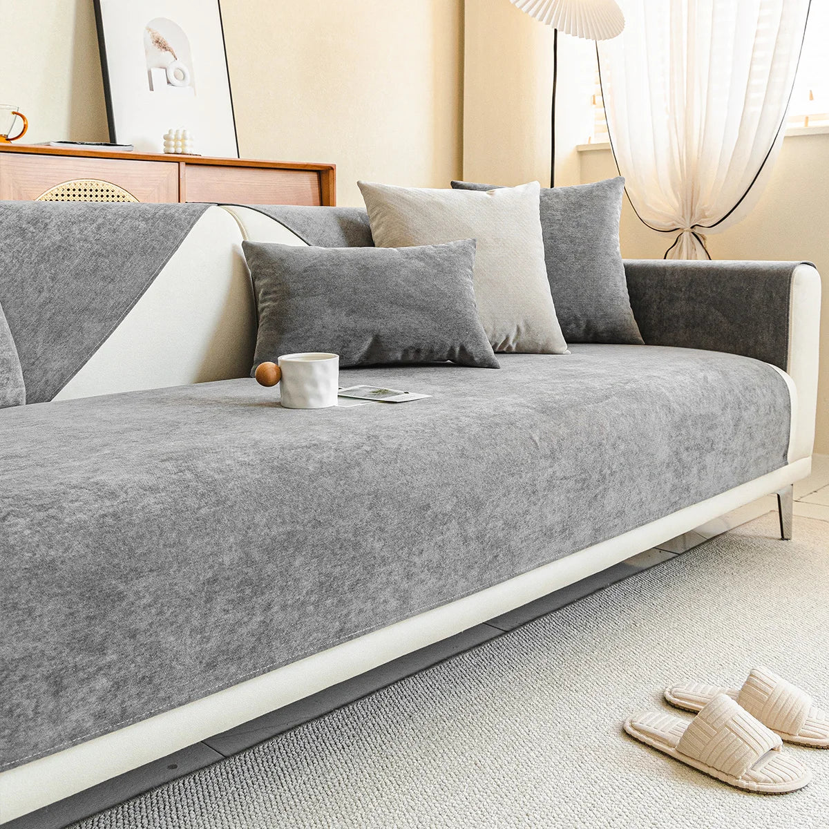 Smooth grey chenille cover on a cream sofa in a bright living room with cushions, a mug and slippers. 10