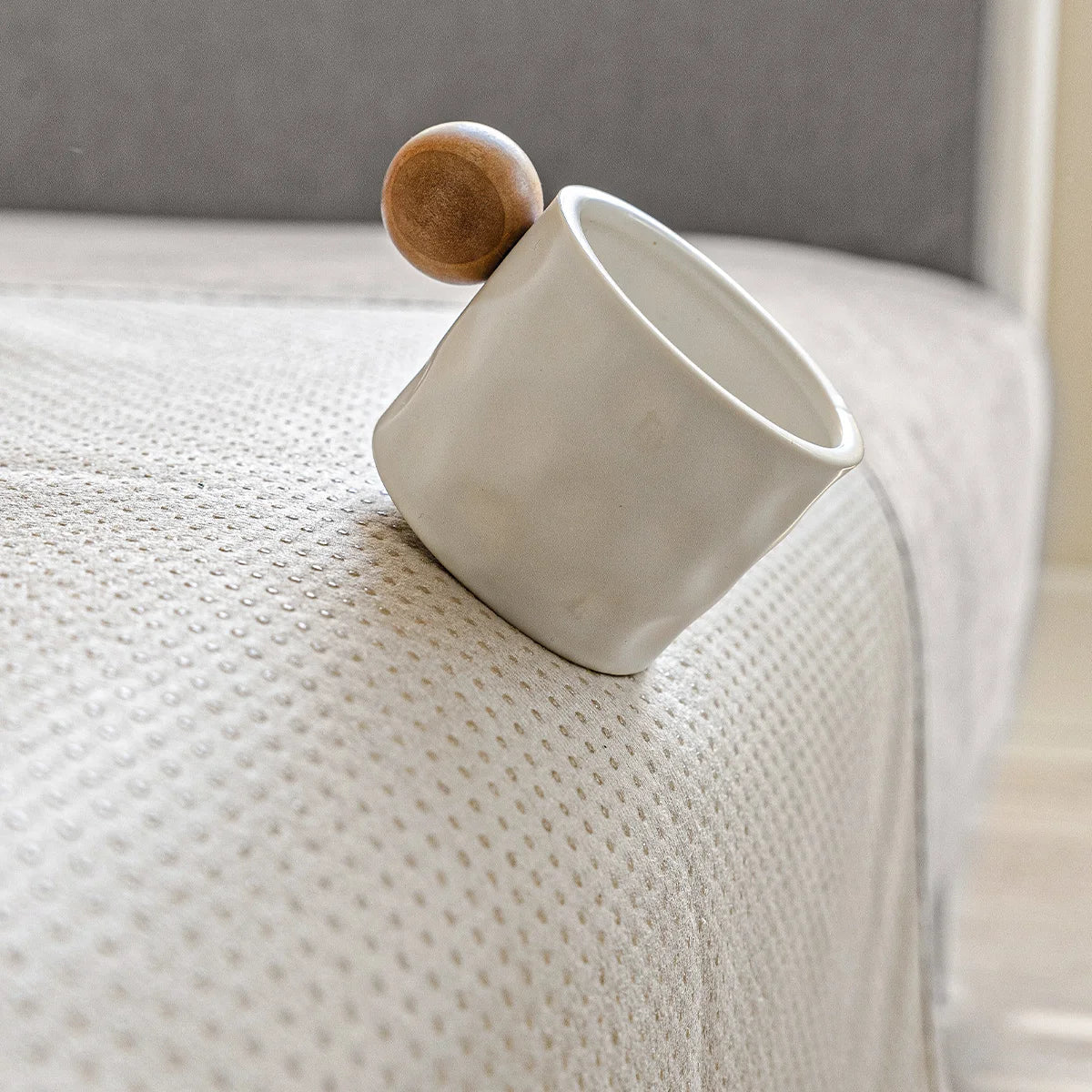 White ceramic mug with wooden ball handle resting on the beige underside of the cover, showing its small non-slip dots. 7