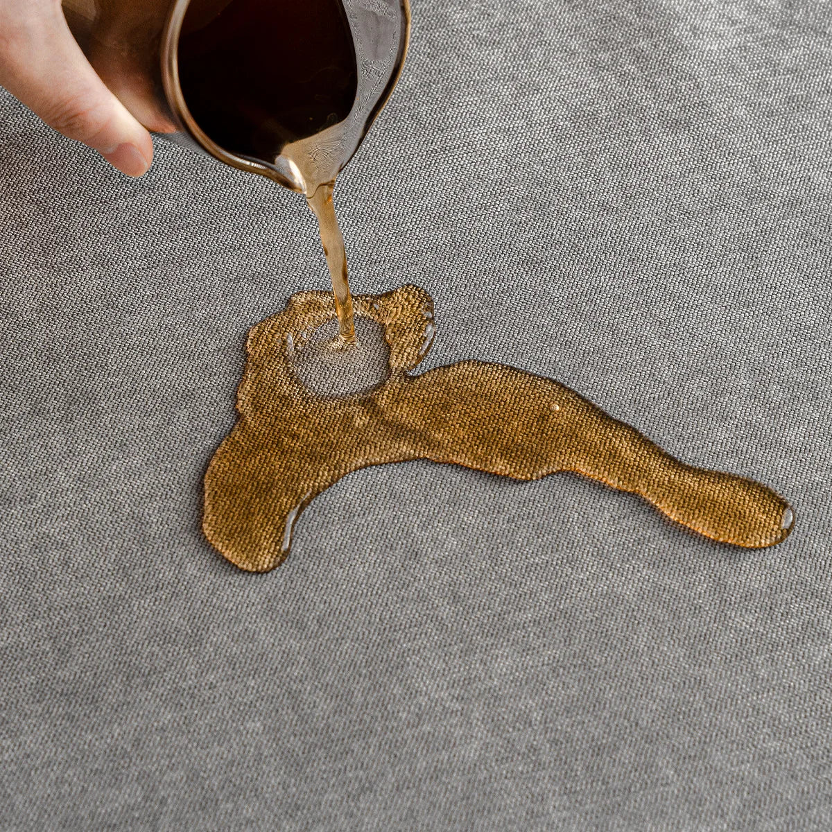 Dark liquid being poured onto grey fabric, pooling on the surface to show it resists spills. 8