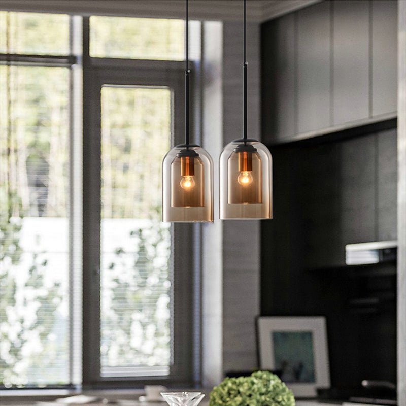 Pair of amber double-glass pendant lights glowing in a kitchen beside a large window 4
