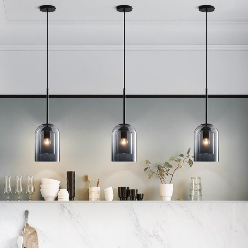 Row of three smoke grey pendants lit above a marble counter with glasses and bowls 5