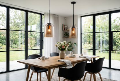 Two amber glass pendants hang above a wooden dining table with black chairs, beside tall glass doors 1