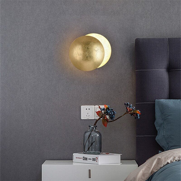 Lamp with smooth gold front disc above a white bedside table with berry stems in a glass vase 7
