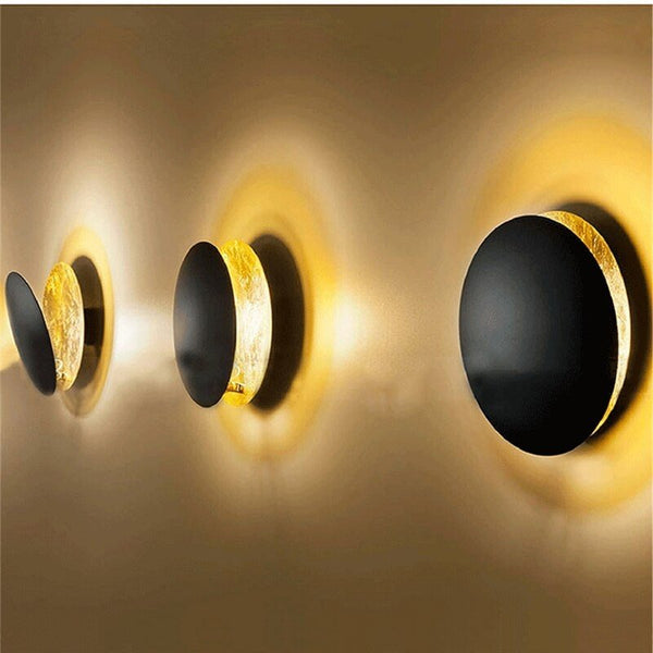 Three black disc lamps seen from the side, gold inner discs casting warm halos on the wall 9