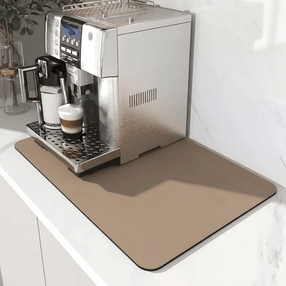 Plain light tan mat under a silver coffee machine on a marble counter, with a latte in the drip tray. 7
