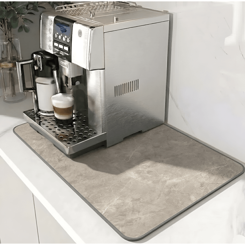 Beige stone-effect mat with a grey edge border, placed under a silver coffee machine on a marble counter. 11