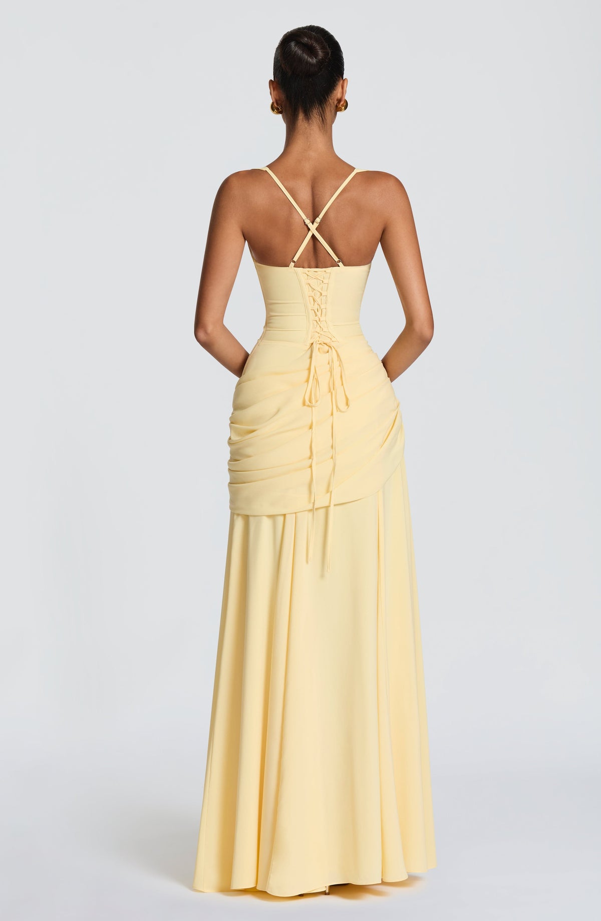 Back view of the pale yellow dress on a model, showing the corset-style lace-up back, crossed thin straps and ruched side drape. 2
