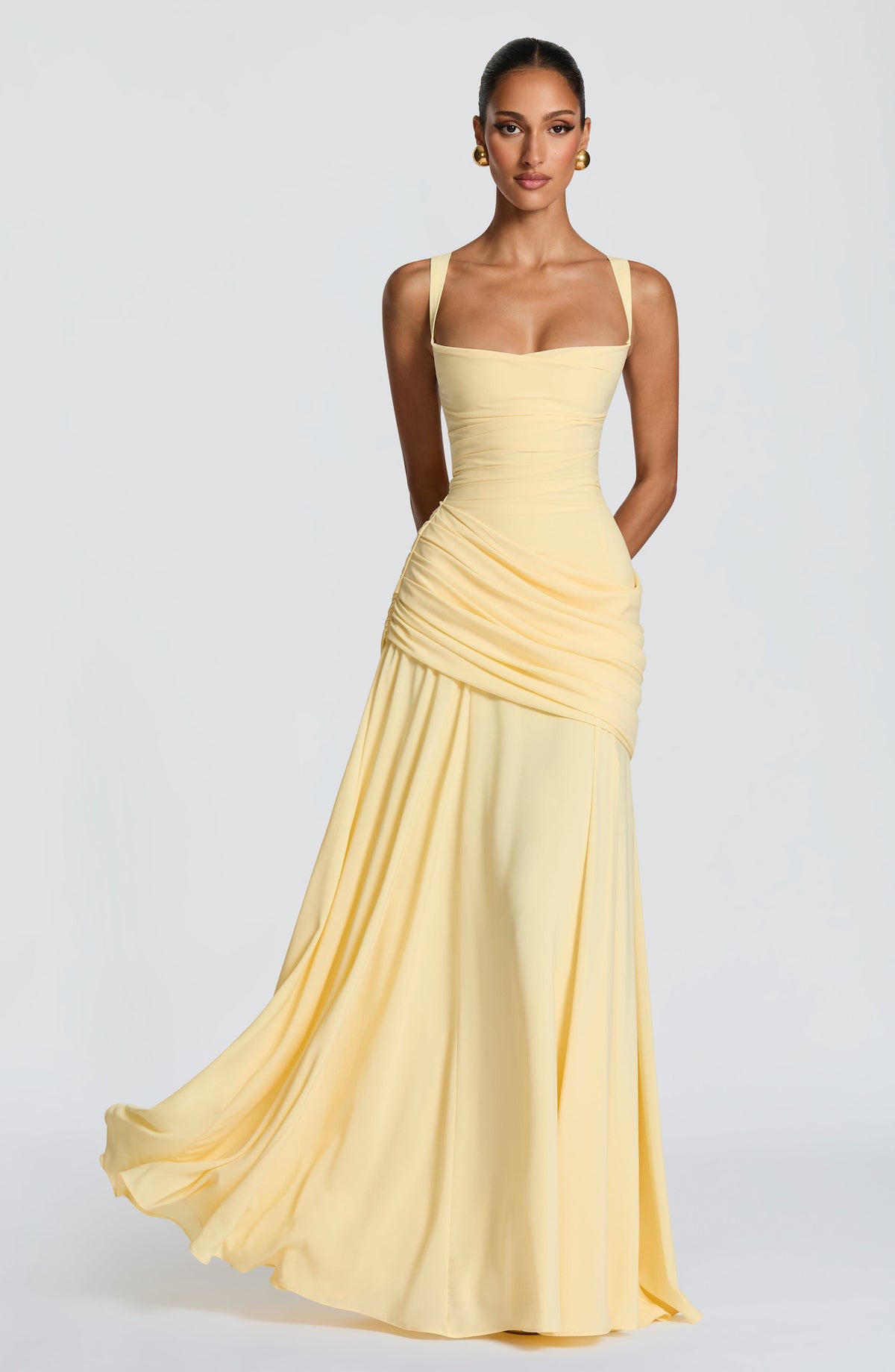 Pale yellow chiffon maxi dress worn by a model, front view, with a ruched asymmetric drape across the hip and flowing skirt. 1