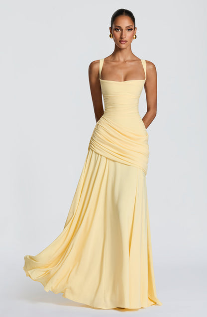 Pale yellow chiffon maxi dress worn by a model, front view, with a ruched asymmetric drape across the hip and flowing skirt. 1