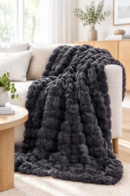 Dark grey bubble-textured plush blanket draped over a cream sofa beside a round wooden coffee table 13