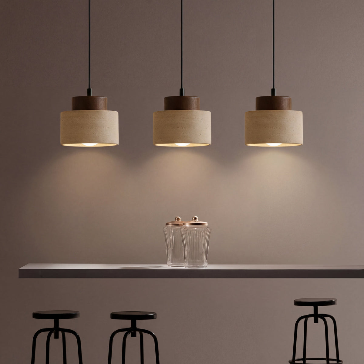Three pendants with visible bulbs cast pools of light above a counter, glass jars and black stools 5