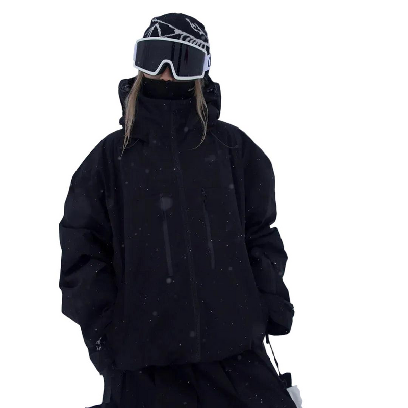 Black version of the jacket worn by a model with a high collar, hood down, goggles and beanie, hands in pockets. 3