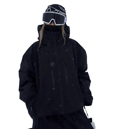 Black version of the jacket worn by a model with a high collar, hood down, goggles and beanie, hands in pockets. 3