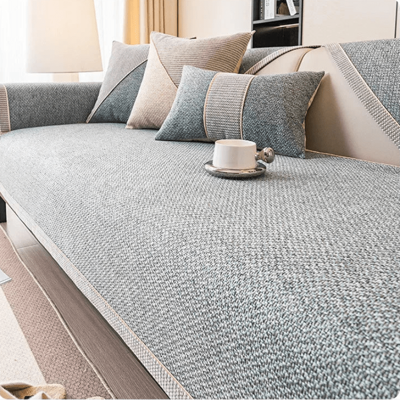 Textured grey woven cover on a sofa seat with a pale braided edge, cushions and a white cup on top. 1