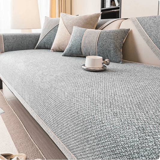Textured grey woven cover on a sofa seat with a pale braided edge, cushions and a white cup on top. 1