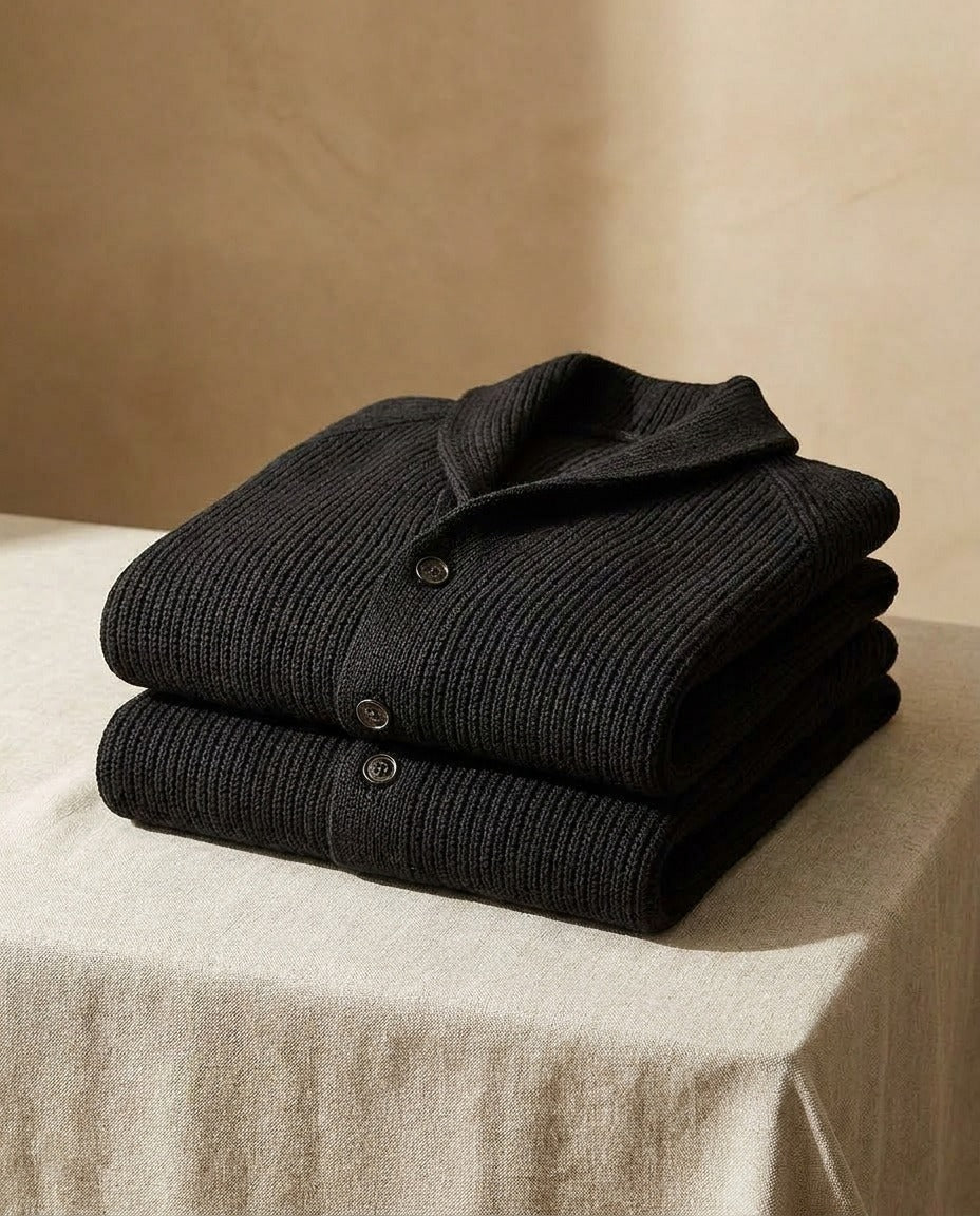 Two black ribbed cardigans folded and stacked on a linen-covered table, showing the shawl collar and buttoned front. 11