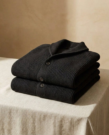 Two black ribbed cardigans folded and stacked on a linen-covered table, showing the shawl collar and buttoned front. 11