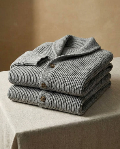 Folded stack of two grey ribbed cardigans on a linen-draped table, showing the shawl collar, brown buttons and ribbed cuff. 9