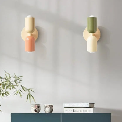 Two wall lamps side by side, one cream and peach, one green and cream, above a teal sideboard with books and small bowls. 14