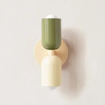 Single wall lamp with a green upper shade, cream backplate and cream lower shade, shown against a plain pale wall. 18