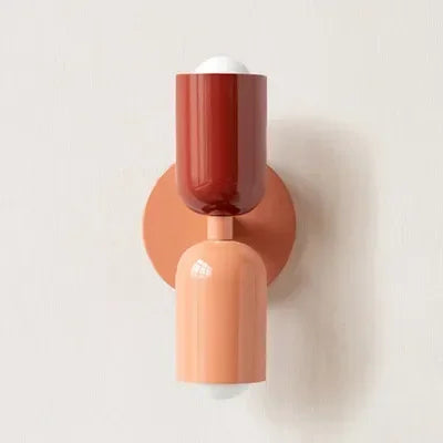 Single wall lamp with a deep red upper shade and peach backplate and lower shade, shown against a plain pale wall. 20