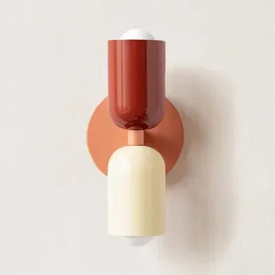 Single wall lamp with a deep red upper shade, peach backplate and cream lower shade, shown against a plain pale wall. 17