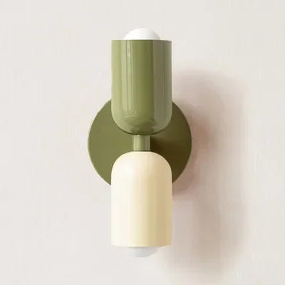 Single wall lamp with a green upper shade and backplate and a cream lower shade, shown against a plain pale wall. 15