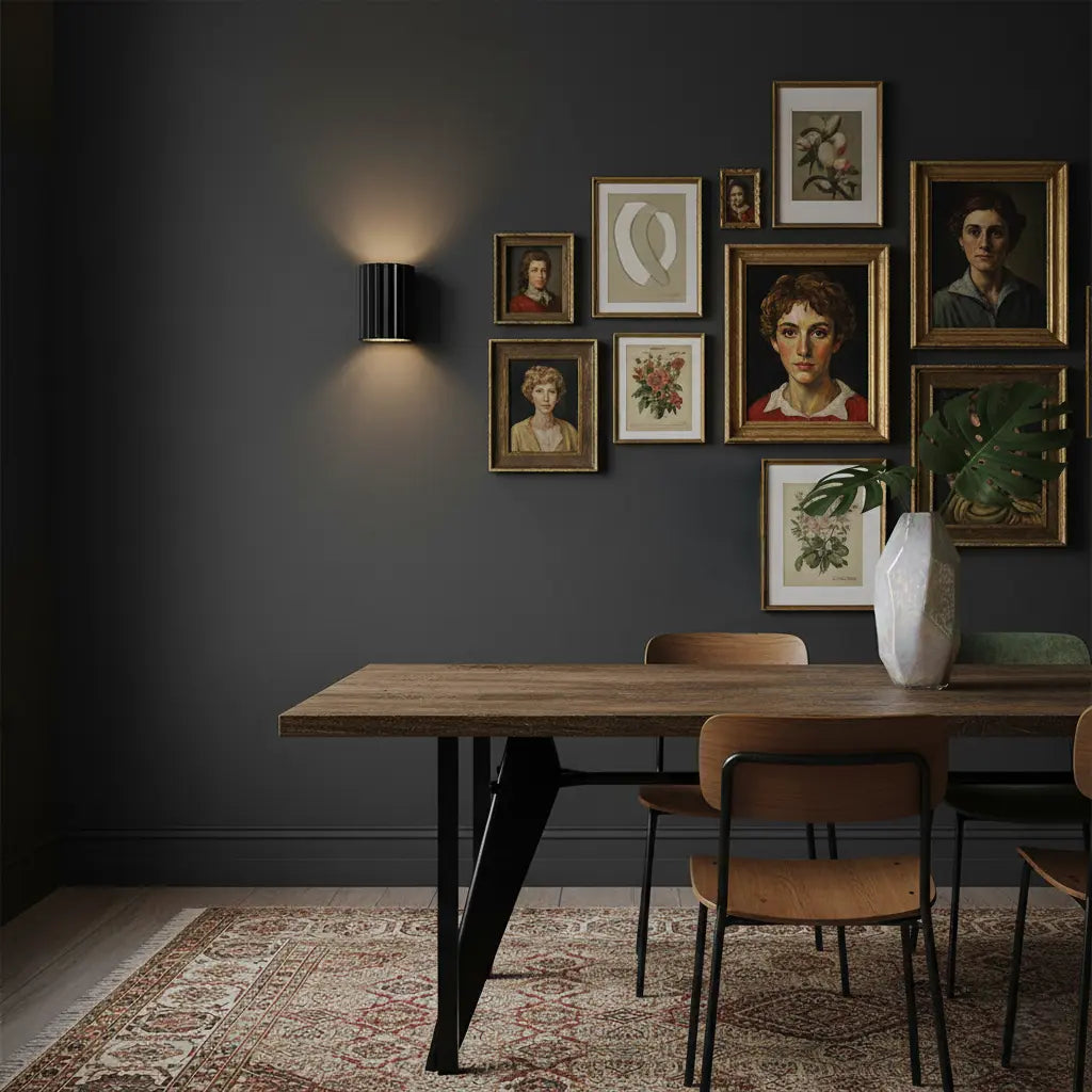 Black fluted wall light on a dark grey wall beside framed portraits above a wooden dining table 6