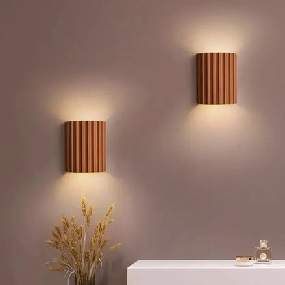 Pair of terracotta fluted wall lights glowing on a mauve wall above dried grasses and a white shelf 8