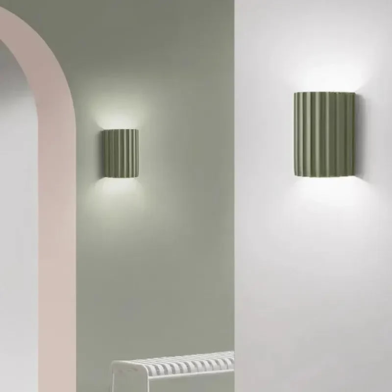 Two sage green fluted wall lights lit on pale walls beside a pink arched doorway 9