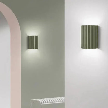 Two sage green fluted wall lights lit on pale walls beside a pink arched doorway 9