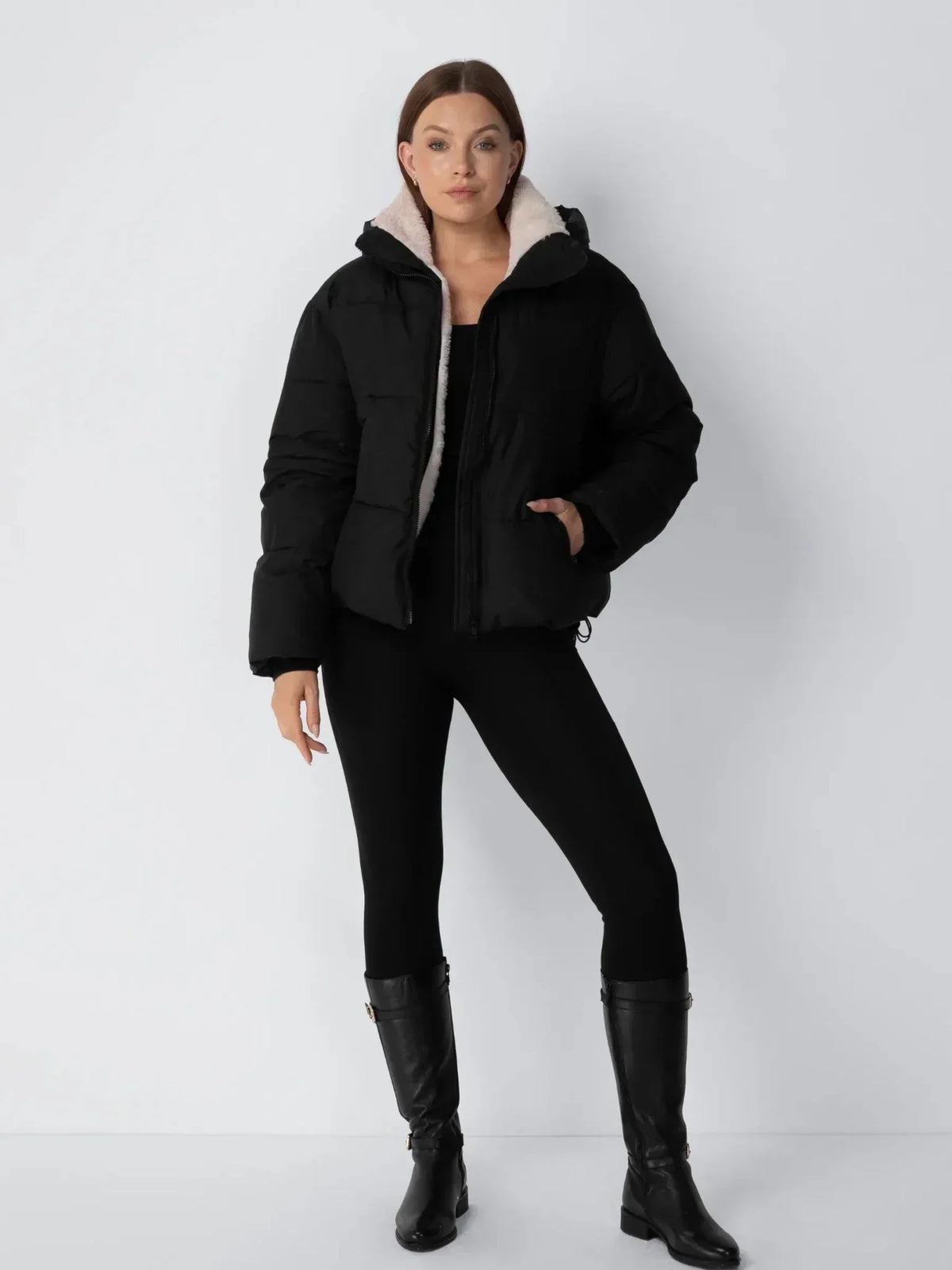 Full-length view of the black puffer jacket with cream fleece collar, worn with black leggings and tall black boots 13