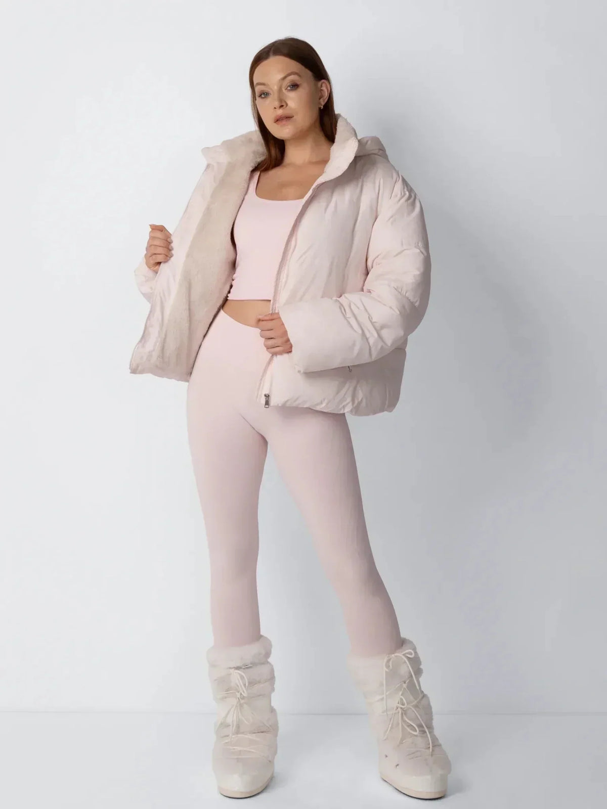 Full-length view of the pale pink puffer jacket held open to show the fleece lining, worn with white fluffy boots 8