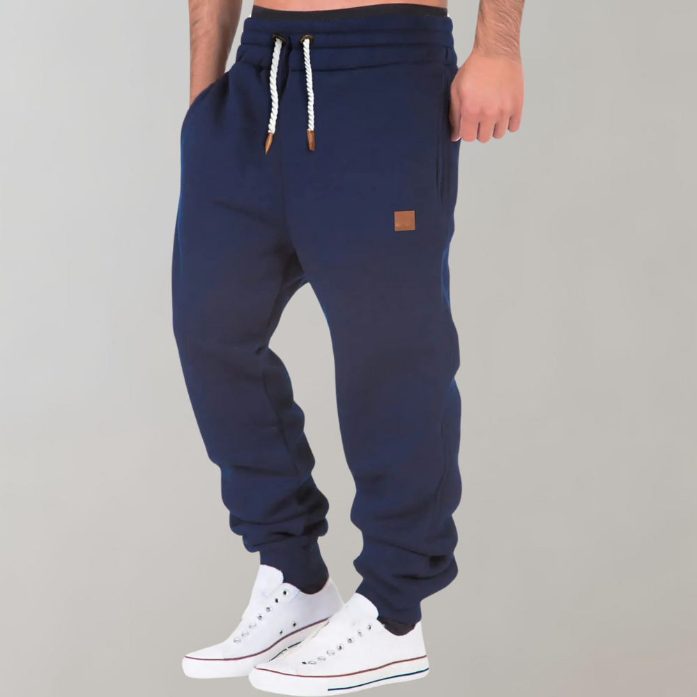 Navy blue joggers worn by a model in white trainers, drawstring waist and tan hip patch 5